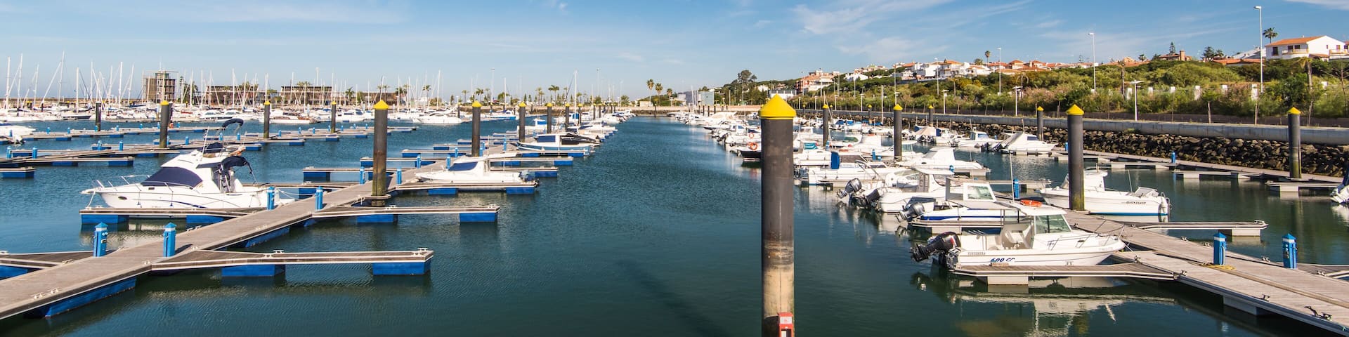 A marina with numerous boats docked, a wooden pier, and a clear blue sky.