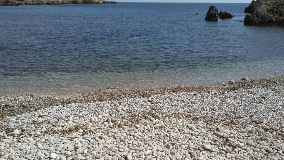A pebbly beach with clear water and rocky outcrops.