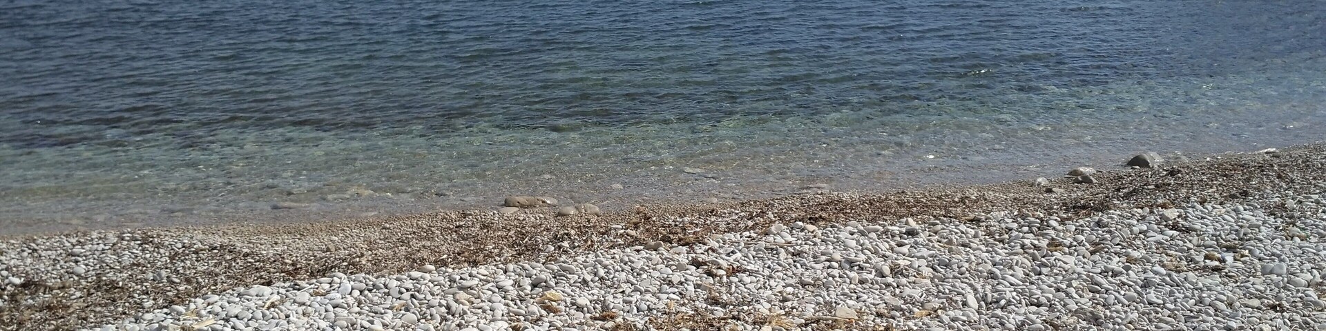 Una playa de adoquines con agua cristalina y afloramientos rocosos.