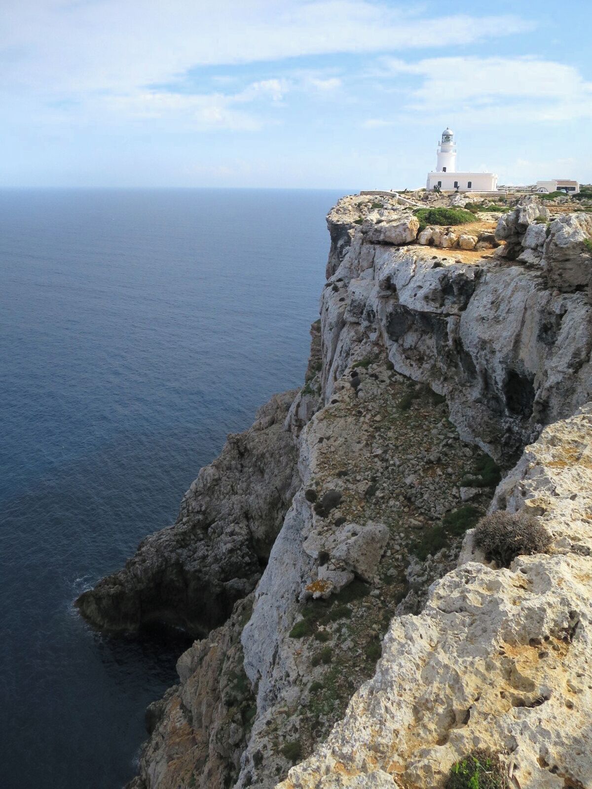A white lighthouse on a rocky cliff overlooking the sea.