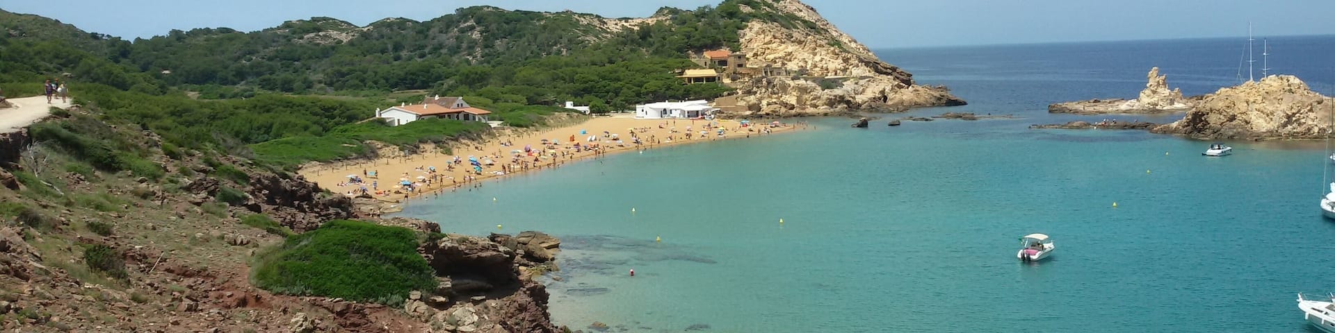 A coastal landscape with a sandy beach, rocky cliffs, and clear turquoise waters.