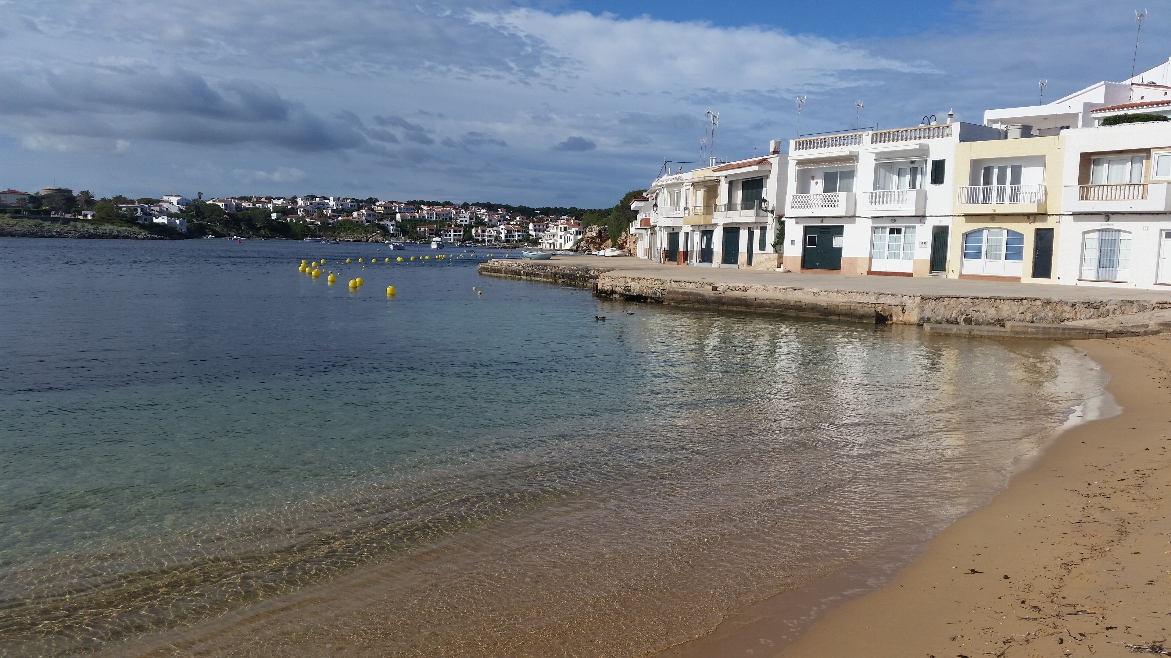 A coastal town with clear waters, a sandy beach, and white buildings with balconies.