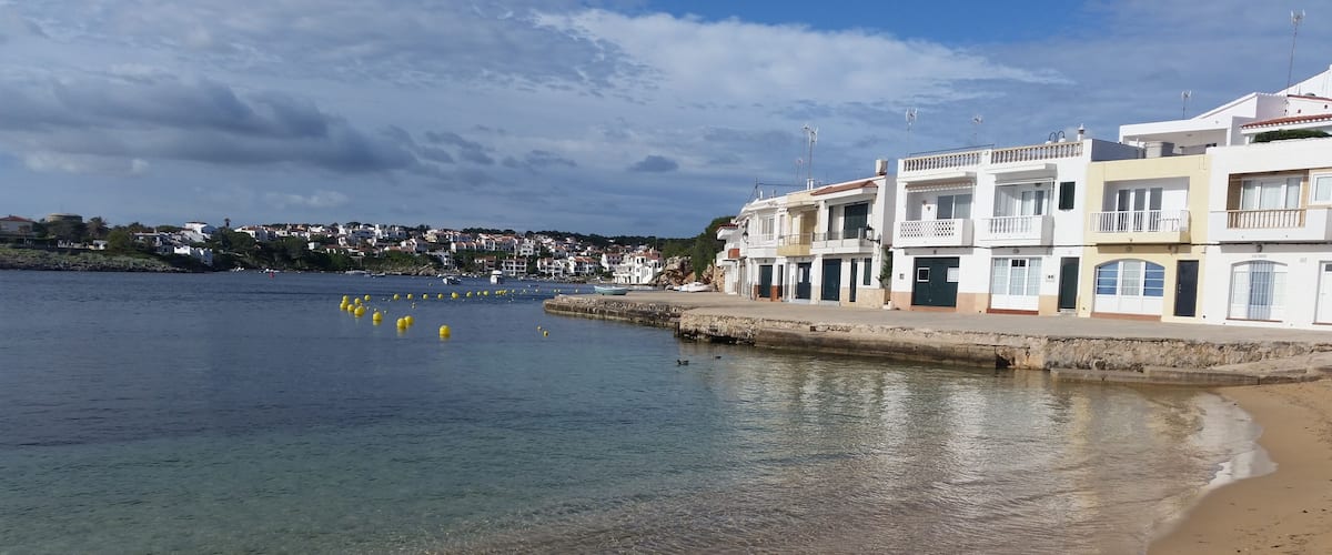 A coastal town with clear waters, a sandy beach, and white buildings with balconies.