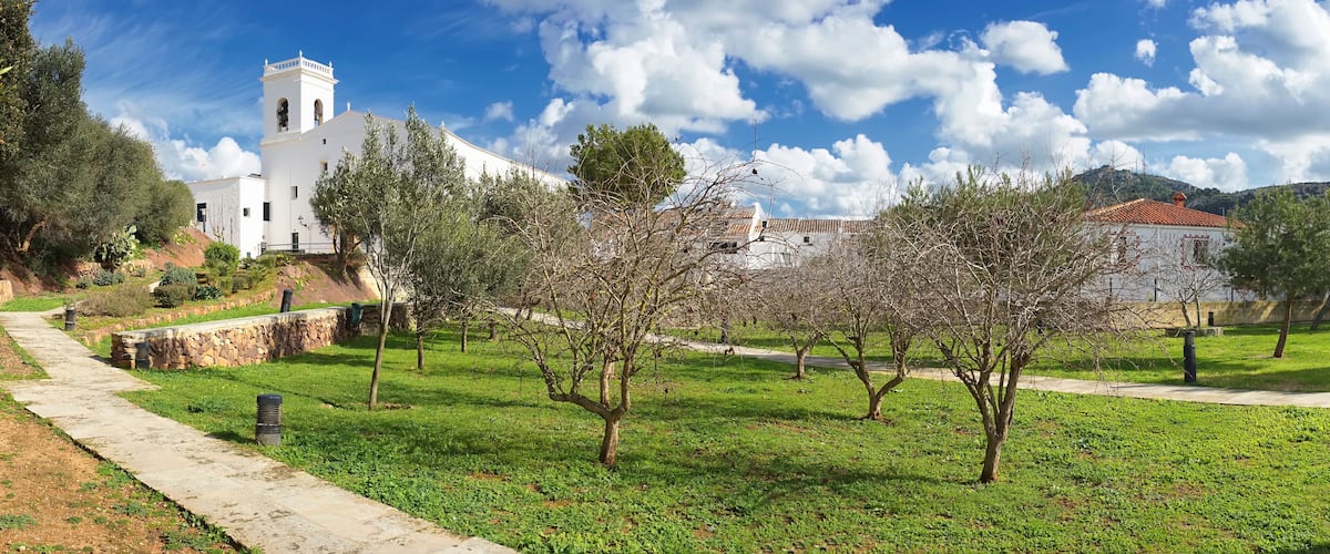 A white church with a bell tower, a stone wall, and a grassy area with trees.