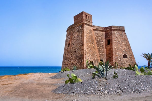 Una fortaleza costera con vista despejada al mar y un primer plano arenoso con cactus.
