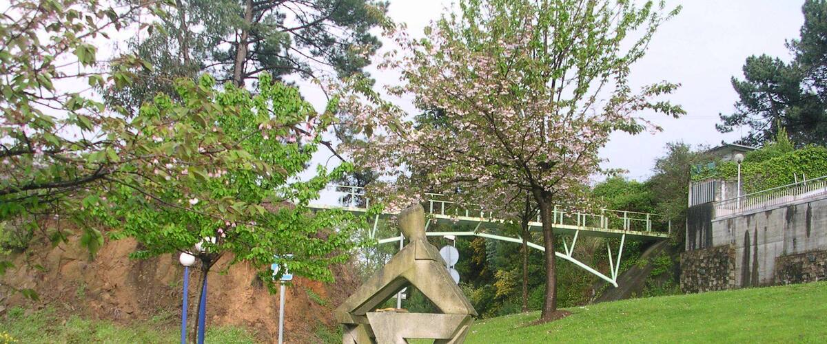 A sculpture of a cyclist on a grassy hill with a bridge and trees in the background.