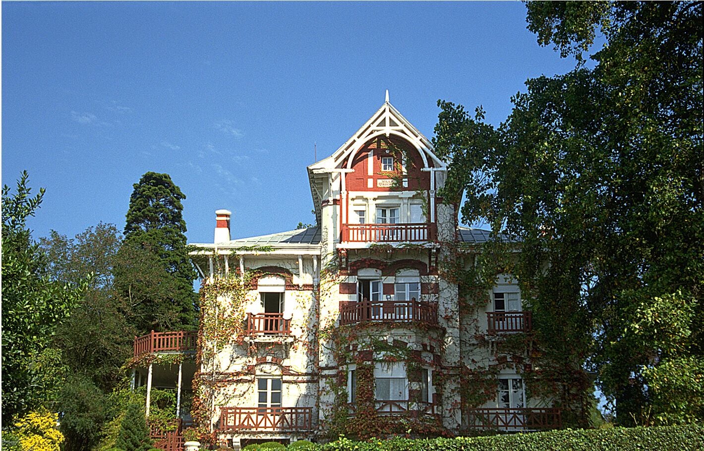 A large, ivy-covered Victorian-style house with multiple balconies and a prominent tower.