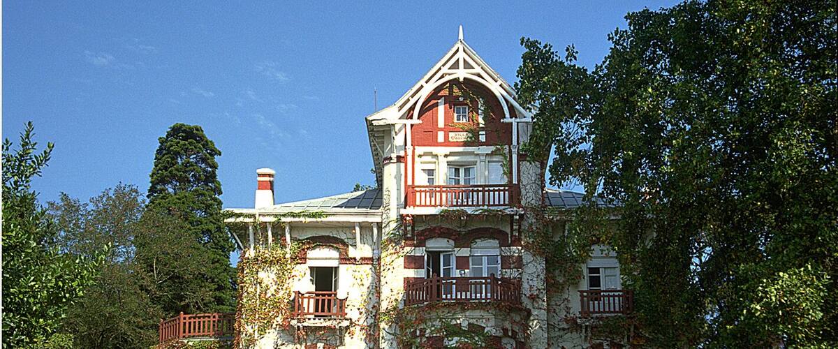 A large, ivy-covered Victorian-style house with multiple balconies and a prominent tower.