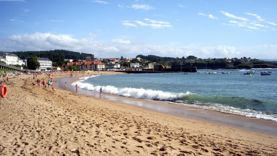 A sandy beach with footprints, a lifebuoy, and boats in the water.