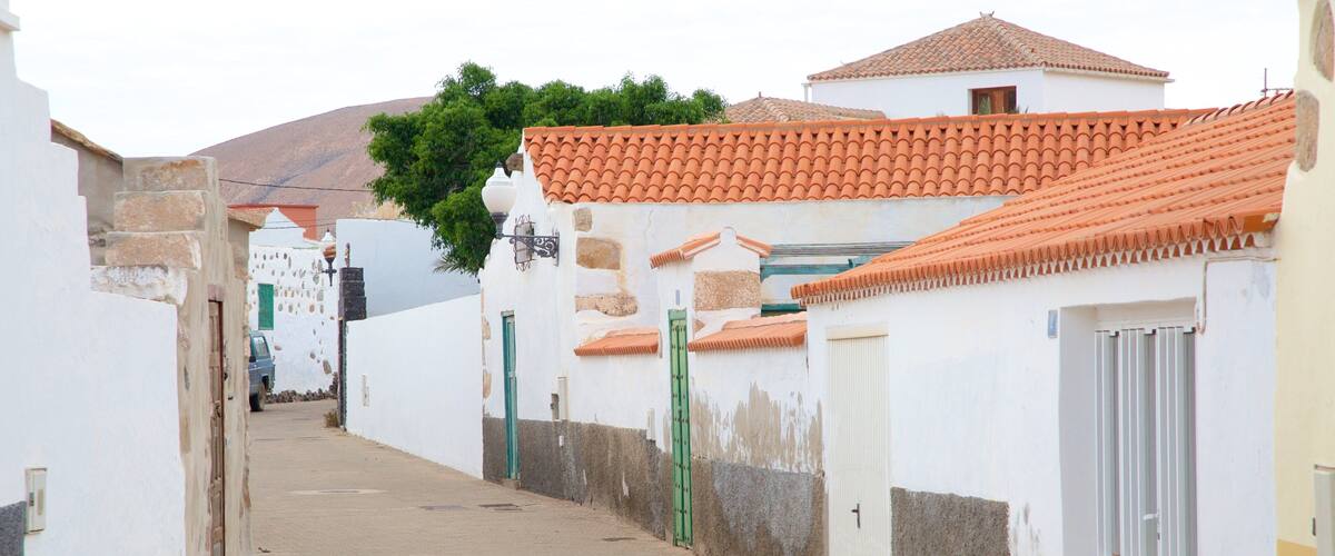 A narrow street with white buildings, red-tiled roofs, and a mountain in the background.