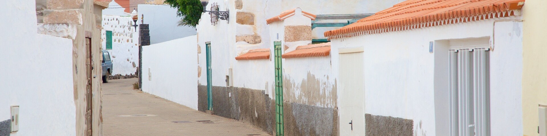 A narrow street with white buildings, red-tiled roofs, and a mountain in the background.