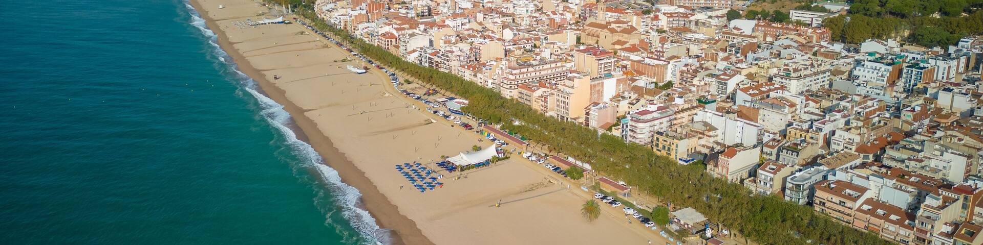 A coastal city with a long sandy beach, dense urban buildings, and rolling hills in the background.