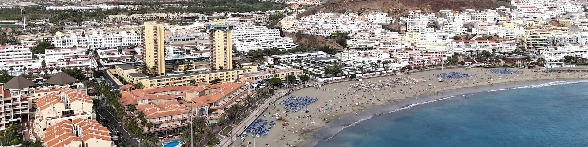 A coastal cityscape with a beach, mountains, and residential buildings.
