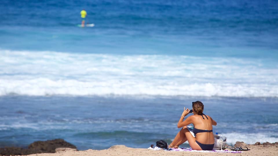 Una mujer con traje de baño sentada sobre una toalla en la playa, cerca del agua.