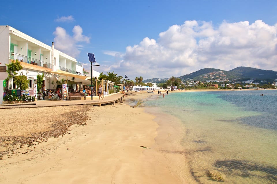 A beach with clear turquoise water, a sandy shore, and a building with a sign reading "ERIA".