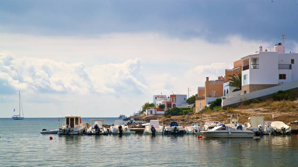 A coastal marina with boats docked, a sailboat in the distance, and buildings along the shore.