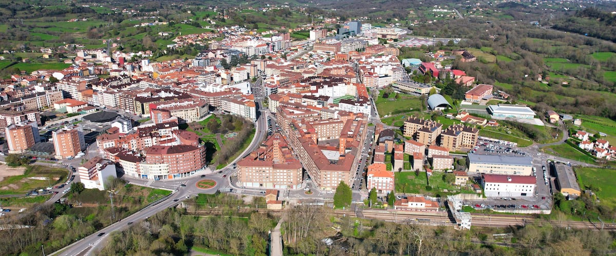 An aerial view of a town with a central square, surrounding buildings, and a mountainous backdrop.