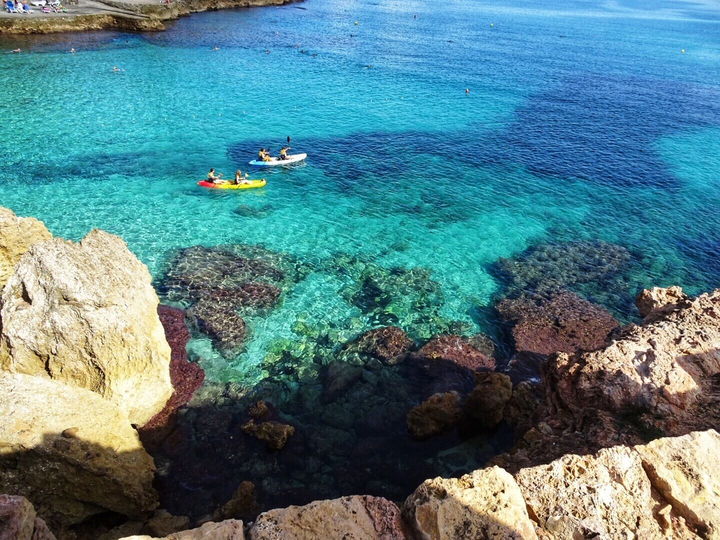 A clear blue sea with rocky shores and kayaks.
