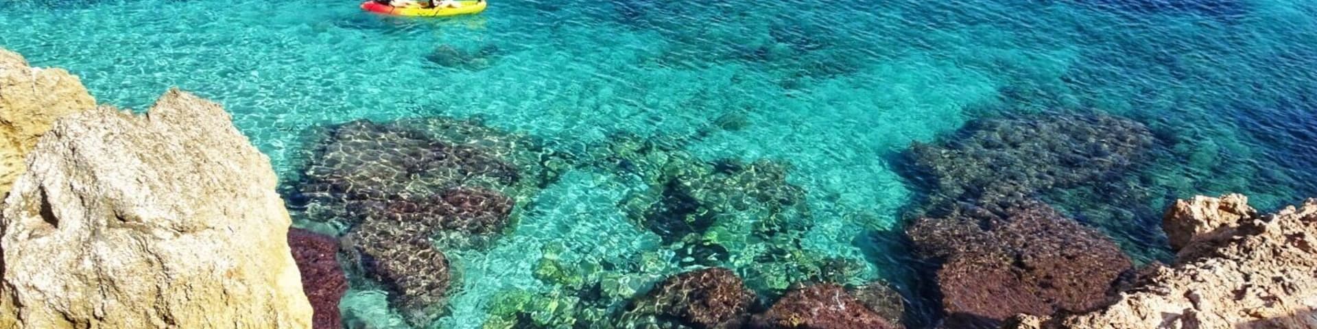 Mar azul límpido com costas rochosas e caiaques.