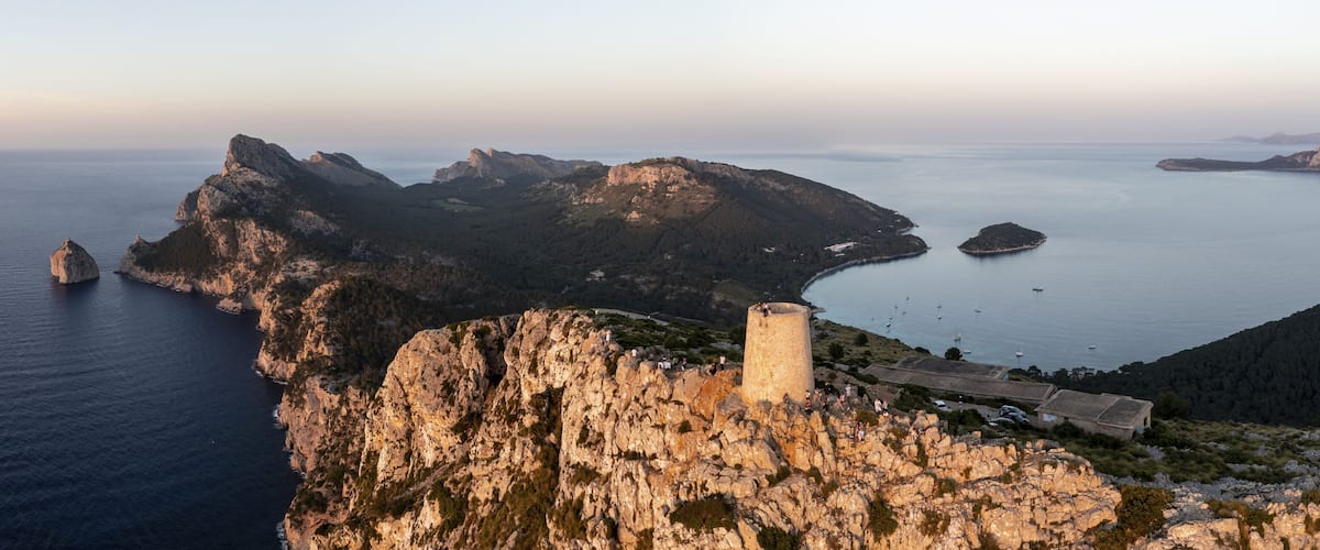 A coastal landscape with rocky cliffs, a lighthouse, and a calm sea.