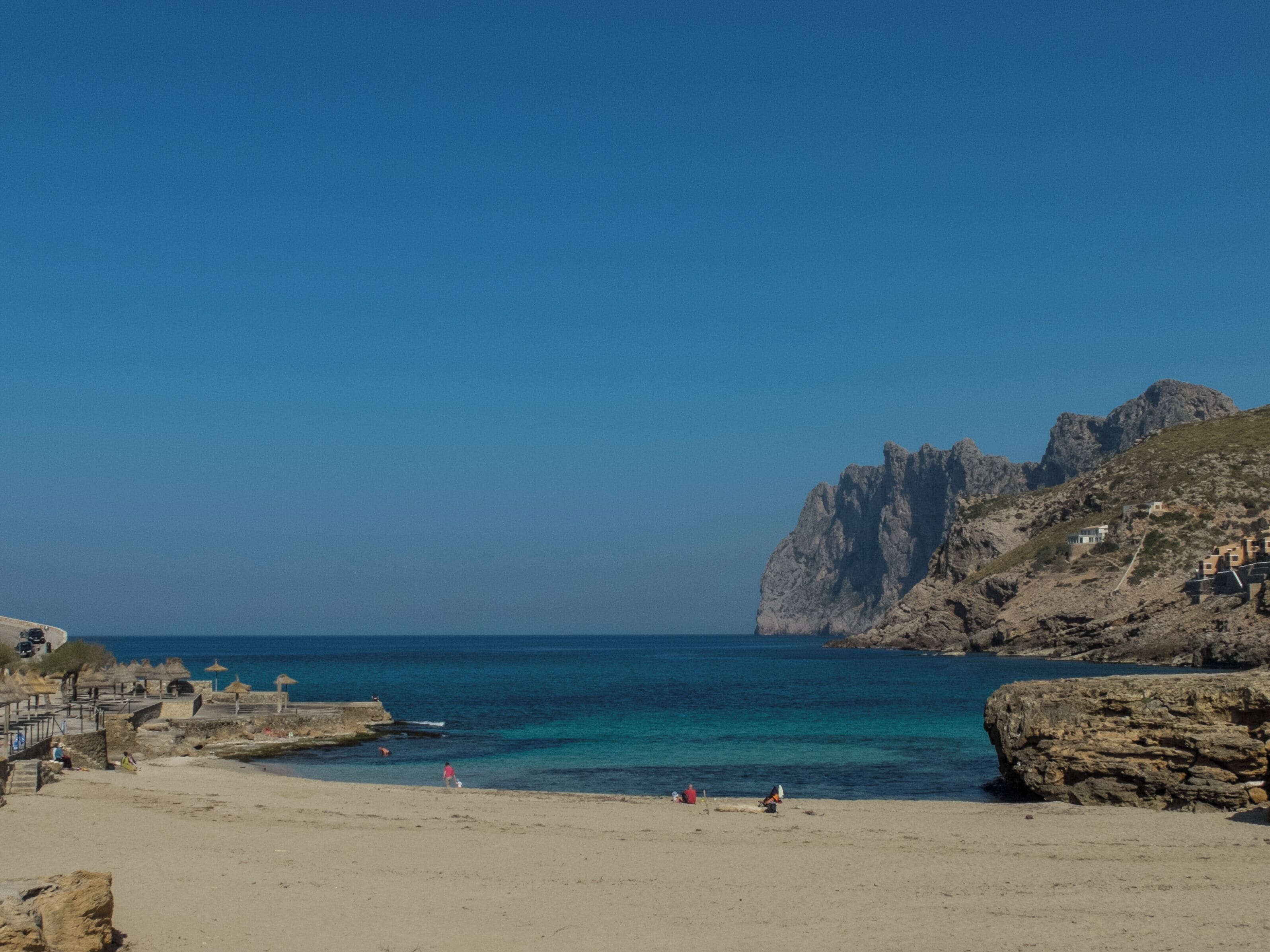 A beach with clear blue water, rocky cliffs, and a few people.