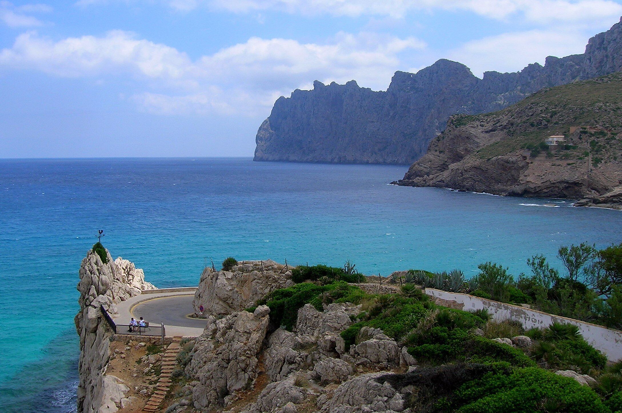 A coastal landscape with a rocky cliff, a winding road, and a clear view of the sea.