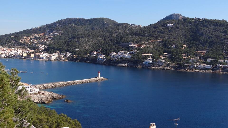 A coastal town with a lighthouse, rocky shoreline, and buildings on hills.