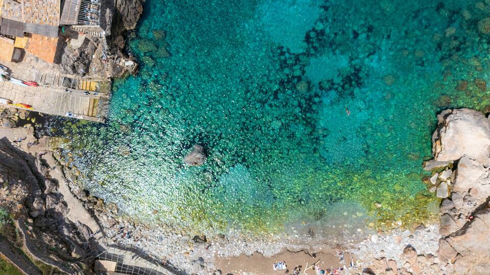 A coastal area with clear turquoise waters, rocky shorelines, and a pedestrian bridge.