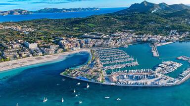 Vista aérea de una ciudad costera con un puerto deportivo, playas y colinas circundantes.