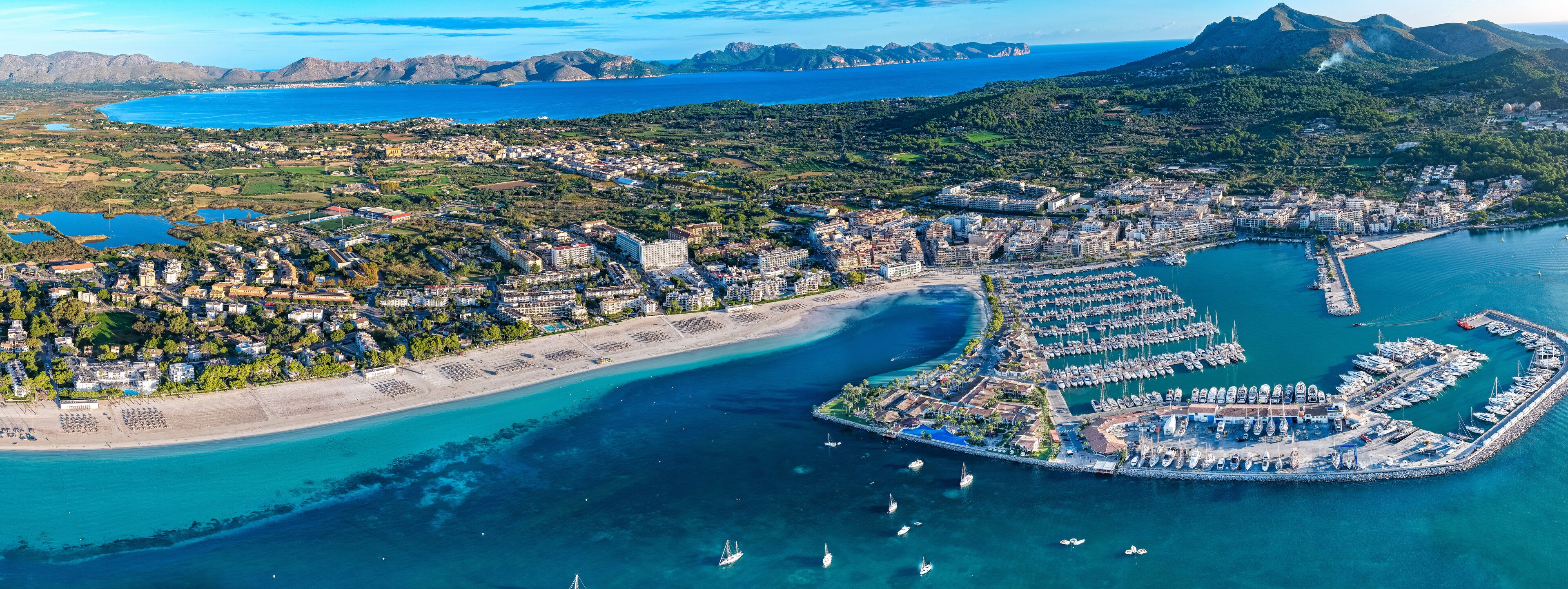 An aerial view of a coastal city with a marina, beaches, and surrounding hills.
