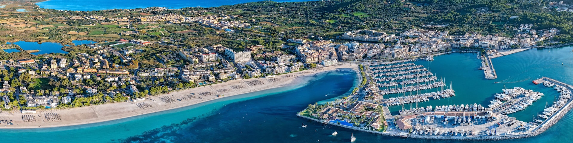 An aerial view of a coastal city with a marina, beaches, and surrounding hills.