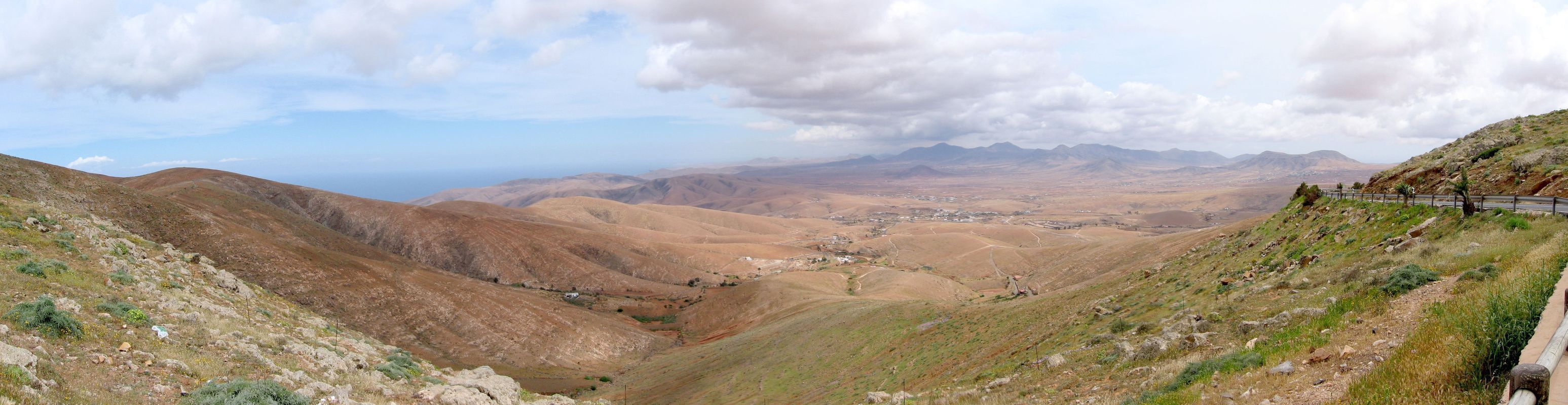 A mountainous landscape with a valley, a road, and distant mountains.