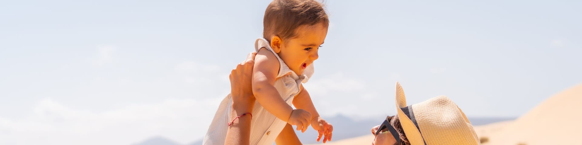 A person holding a child in a desert with sand dunes and mountains in the background.