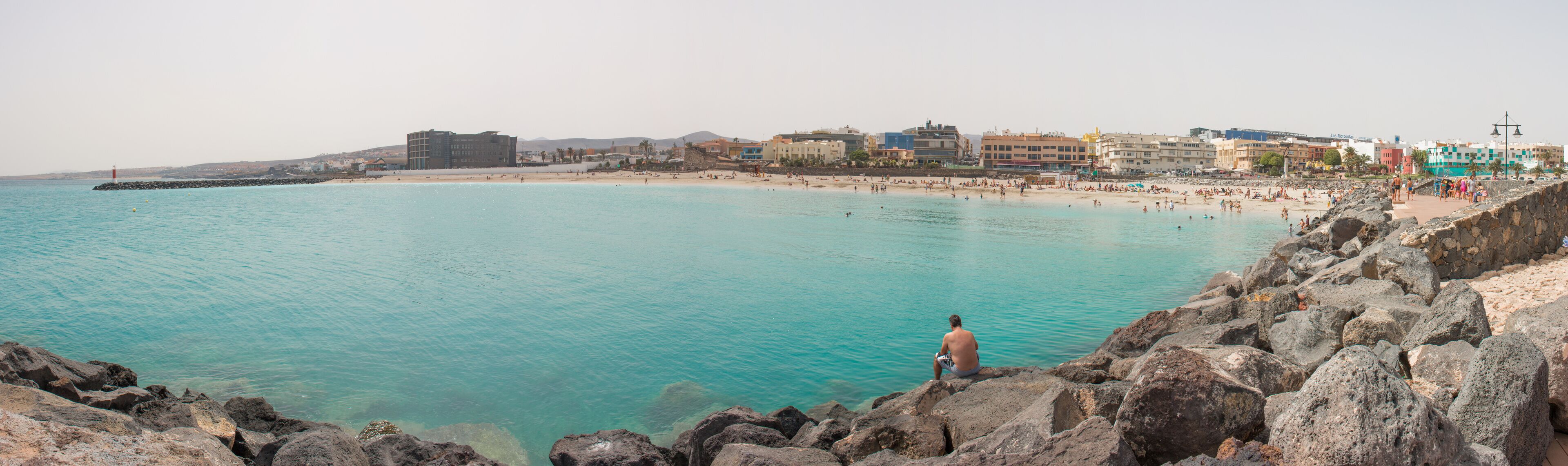 Un paisaje costero con playa, costa rocosa y edificios a lo largo de la orilla.