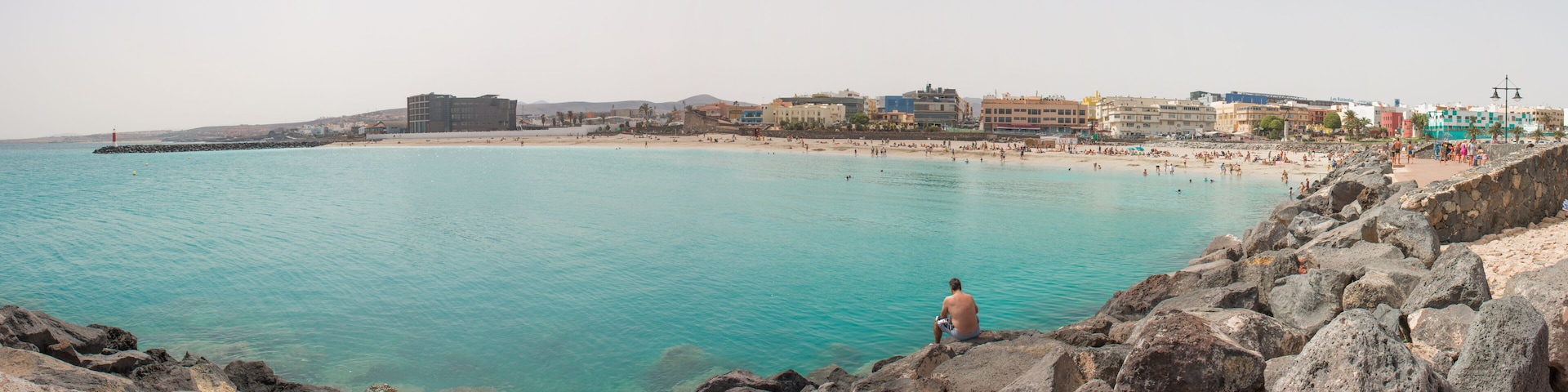 Un paisaje costero con playa, costa rocosa y edificios a lo largo de la orilla.