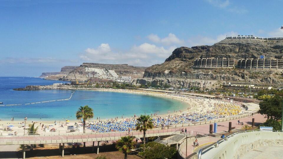 A coastal city with a beach, a rocky shoreline, and a large building on a hill.