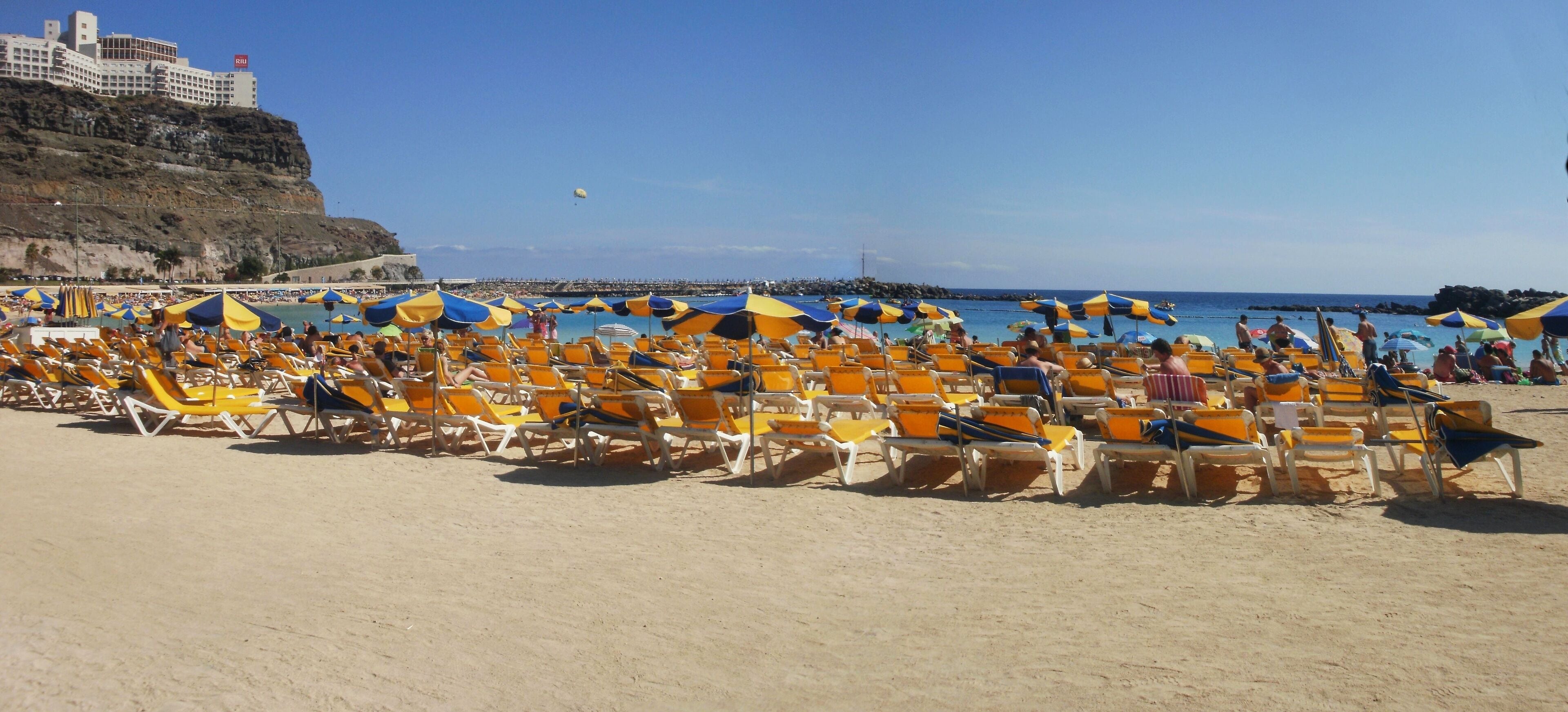 A beach with numerous yellow and blue beach umbrellas and sun loungers.