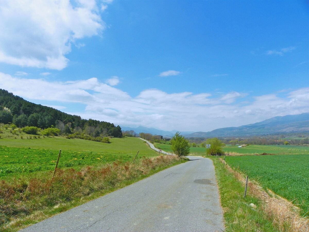 A rural road winding through green fields with distant hills under a clear sky.