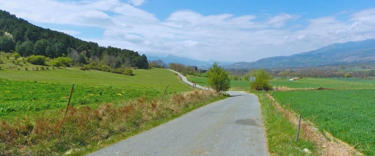 A rural road winding through green fields with distant hills under a clear sky.