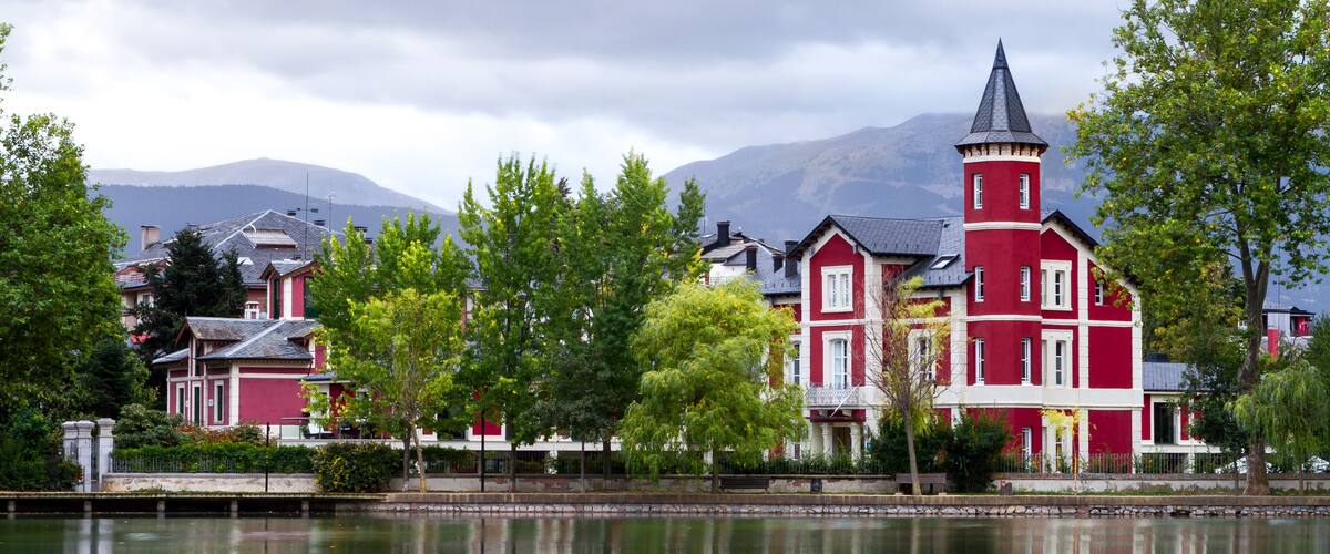 A red building with a tower by a calm lake, surrounded by trees and mountains.