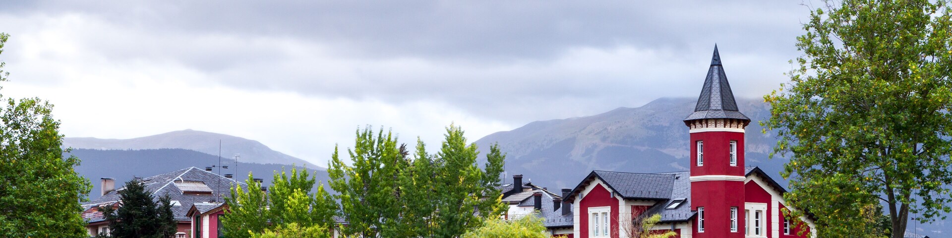 A red building with a tower by a calm lake, surrounded by trees and mountains.