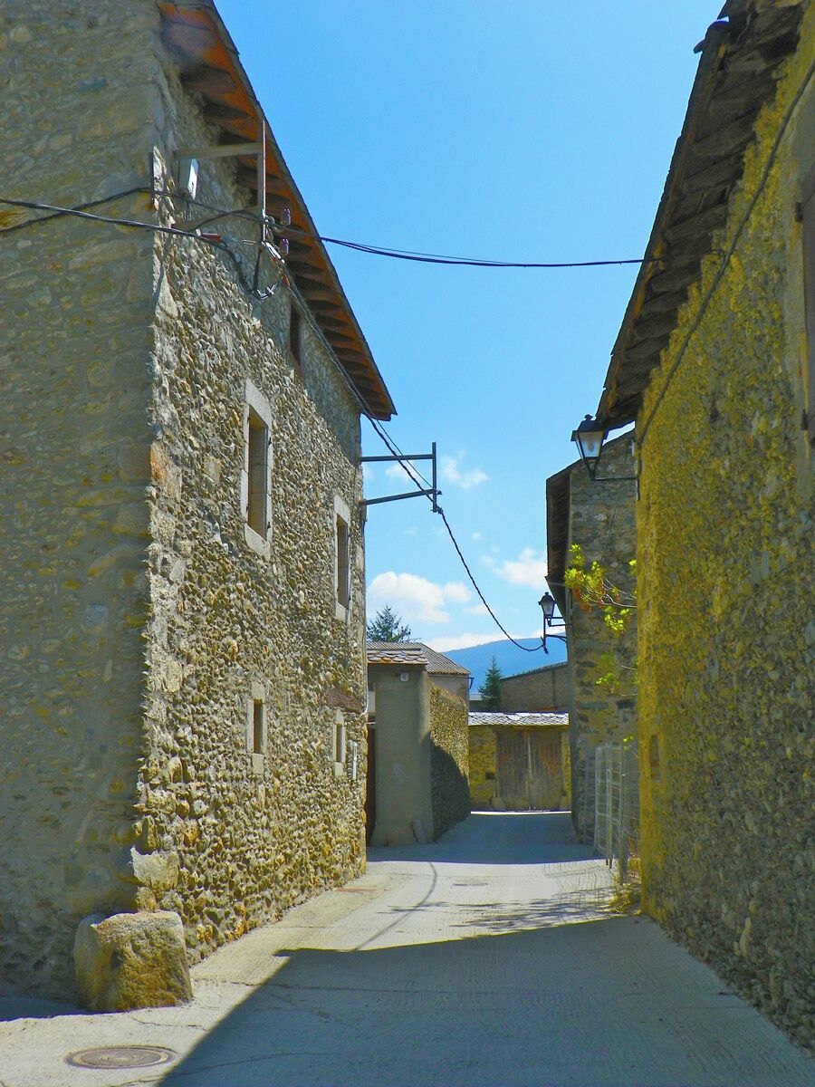 A narrow stone street flanked by buildings with small windows and a clear blue sky.