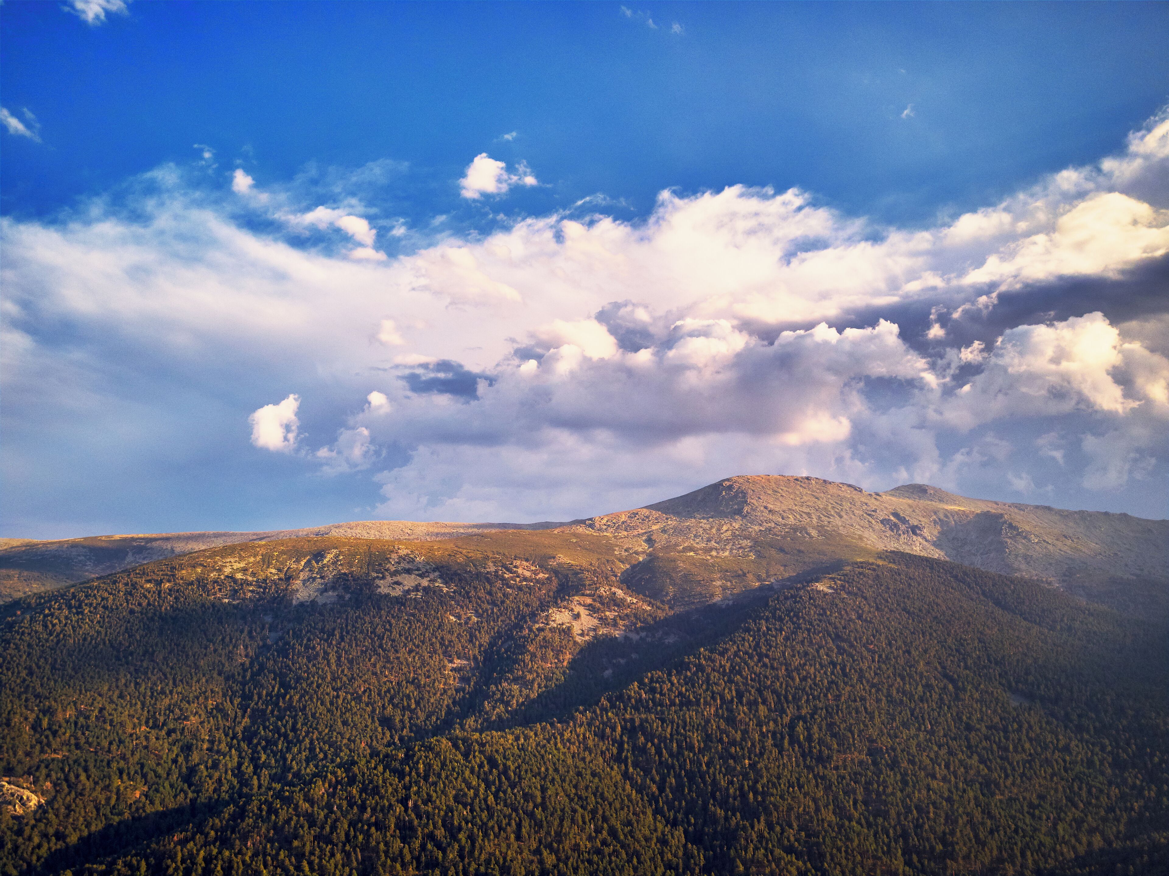 Eine gebirgige Landschaft mit dichten Wäldern und einem klaren Himmel mit vereinzelten Wolken.