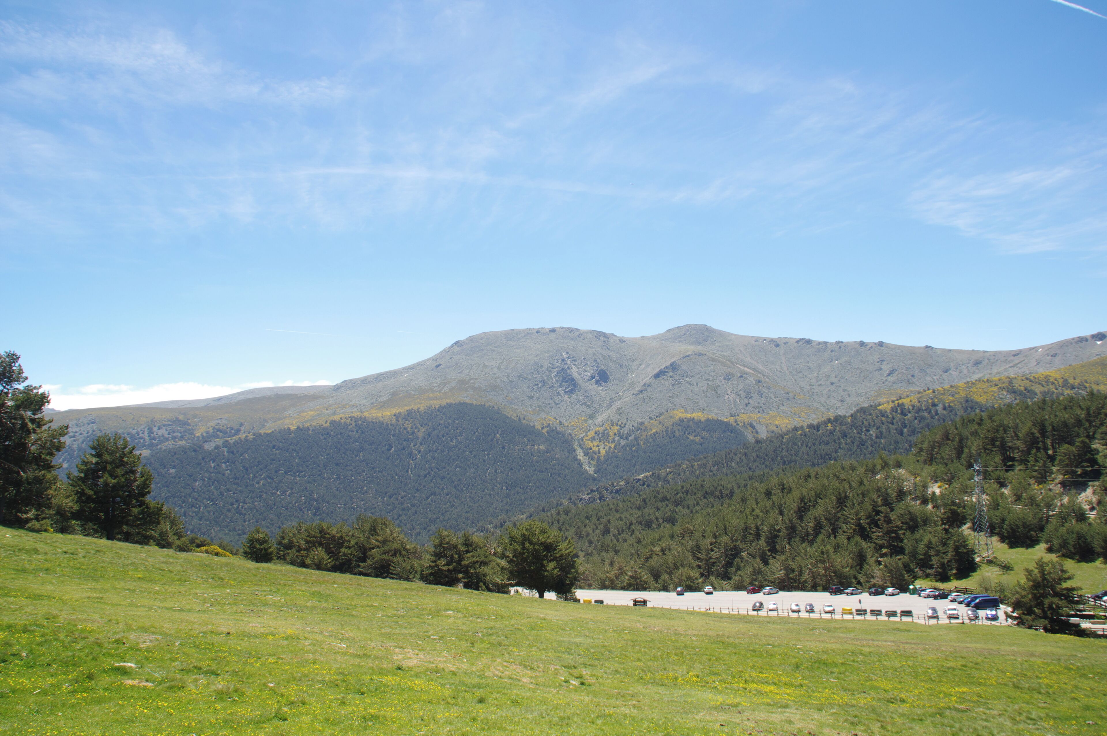 A mountainous landscape with a clear sky, a parking lot, and a building in the foreground.