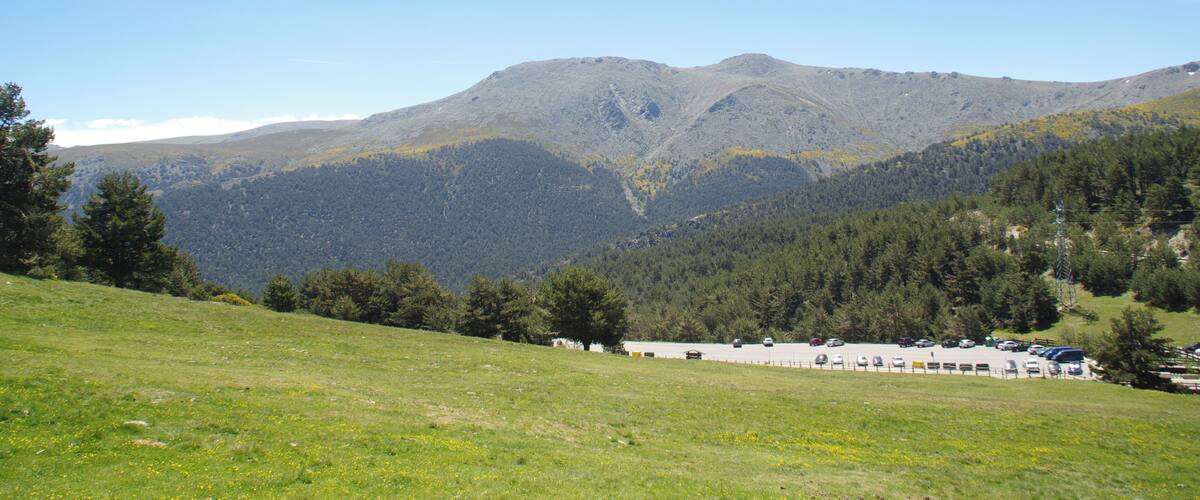 A mountainous landscape with a clear sky, a parking lot, and a building in the foreground.
