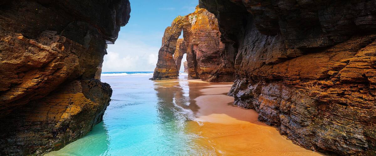 A natural rock arch formation over a beach with clear turquoise water.