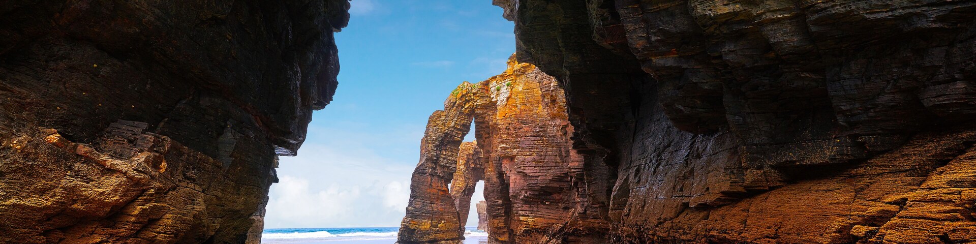 A natural rock arch formation over a beach with clear turquoise water.