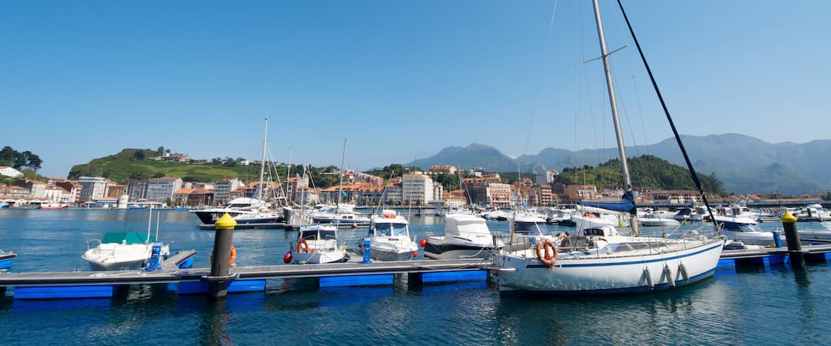 A marina with various boats docked, a clear blue sky, and a mountainous landscape in the background.