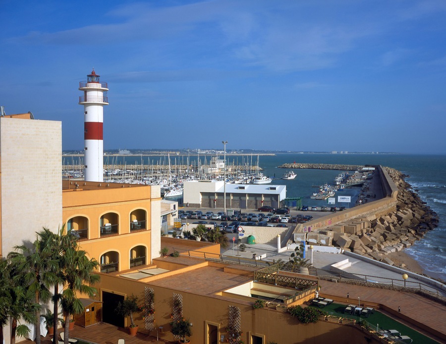 Una marina costera con barcos, un faro y un litoral rocoso.