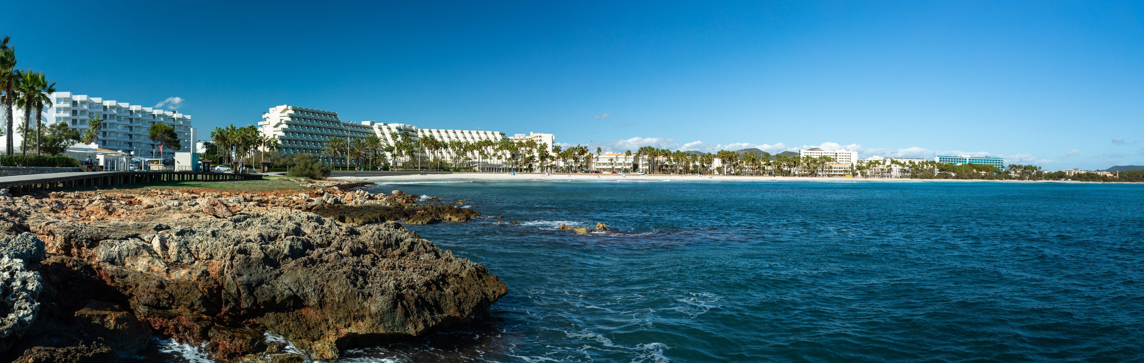A coastal resort with a rocky shoreline, palm trees, and beachfront hotels.